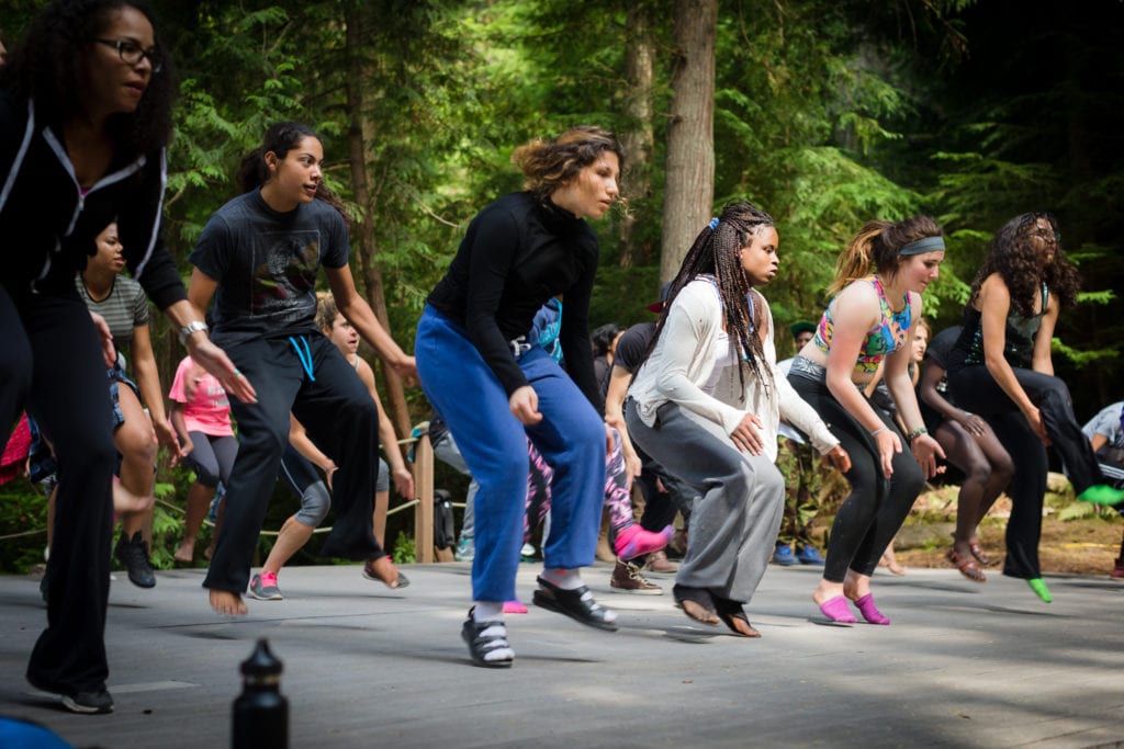 A large group of students in the woods performing a coordinated dance at Partners for Youth's Power of Hope summer camp 