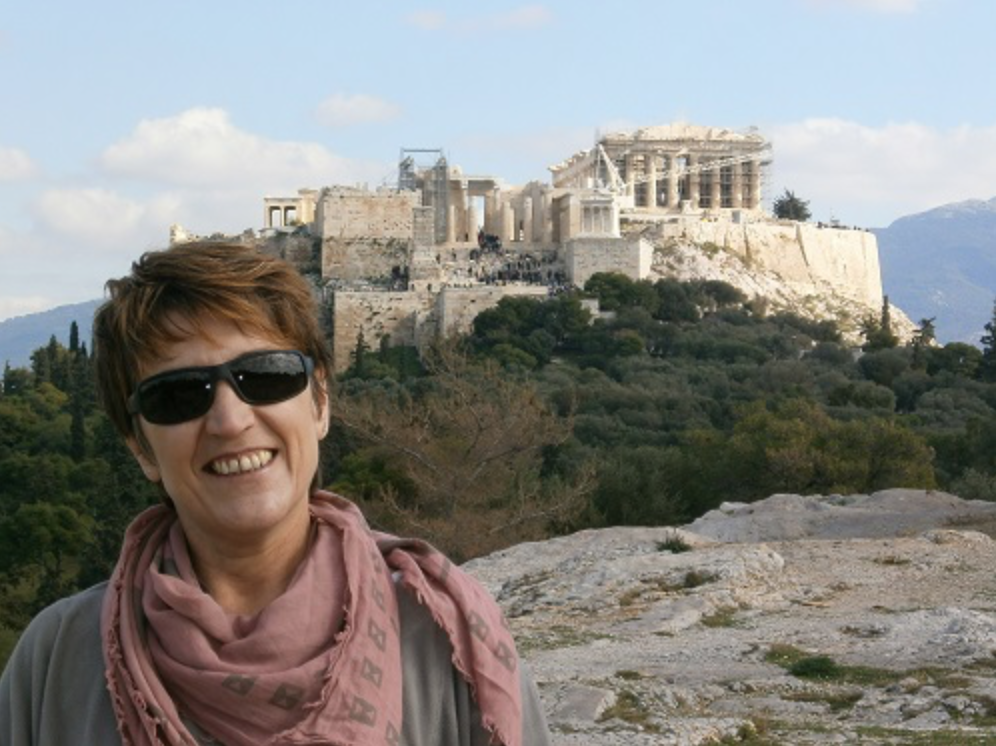 Creative Classroom participant Kleopatra Kalogerakou stands on a ridge, an ancient greek temple stands behind her off in the distance